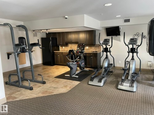 This fitness area features a variety of exercise equipment and a kitchenette with dark wood cabinetry and a black refrigerator - Edmonton, AB - Indoor Photo Showing Gym Room
