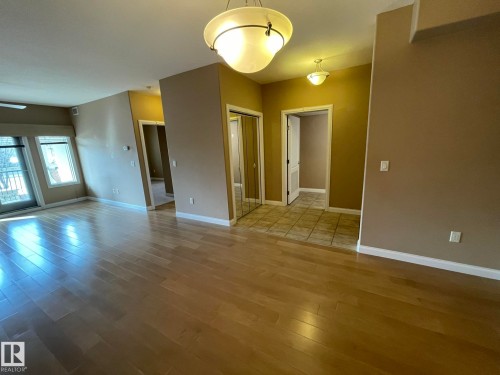 This inviting living area features light-toned hardwood flooring, light tan walls, and a window with a glass door providing natural light - Edmonton, AB - Indoor Photo Showing Other Room