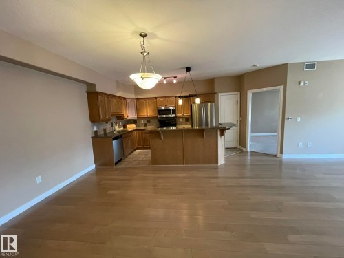 Open concept living area featuring light-toned flooring, a kitchen with wooden cabinetry, stainless steel appliances, and a breakfast bar - Edmonton, AB - Indoor Photo Showing Kitchen