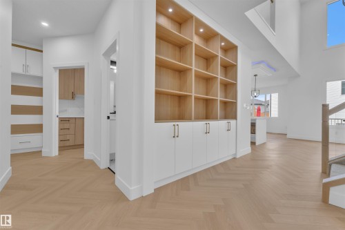 The property features herringbone wood flooring, built-in shelving with integrated lighting, white cabinetry with gold-toned hardware, and a high ceiling - 12 Dalquist Bay, Leduc, AB - Indoor Photo Showing Other Room