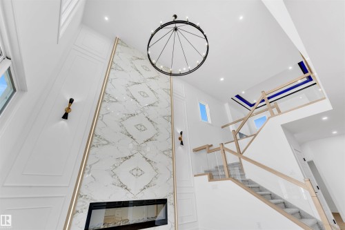 This property features a grand living space with a tall ceiling, a prominent marble-patterned accent wall with an integrated fireplace, and a striking circular chandelier - 12 Dalquist Bay, Leduc, AB - Indoor Photo Showing Other Room With Fireplace