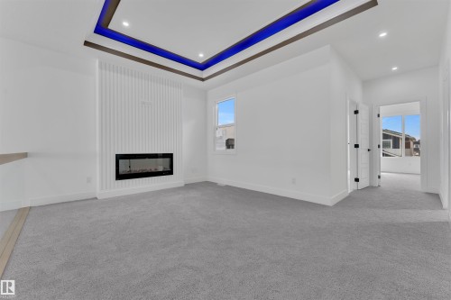 This room features a contemporary fireplace, plush carpeting, a window providing natural light, and a tray ceiling with accent lighting - 12 Dalquist Bay, Leduc, AB - Indoor With Fireplace