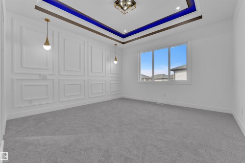 The spacious room features light grey carpeting, white walls with decorative paneling, and a large window providing natural light - 12 Dalquist Bay, Leduc, AB - Indoor Photo Showing Other Room