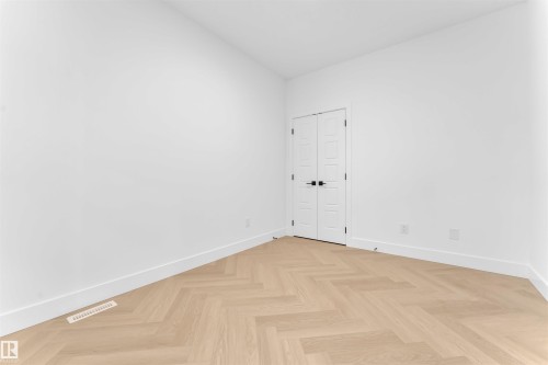 Room featuring light-colored hardwood floors with a herringbone pattern, white walls, and white double doors with black hardware - 12 Dalquist Bay, Leduc, AB - Indoor Photo Showing Other Room