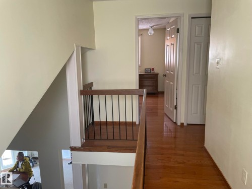 Upper-level hallway featuring wood-finish flooring, a white paneled door, and a staircase with a wood-finish handrail and black metal spindles - 9320 175 Street, Edmonton, AB - Indoor Photo Showing Other Room