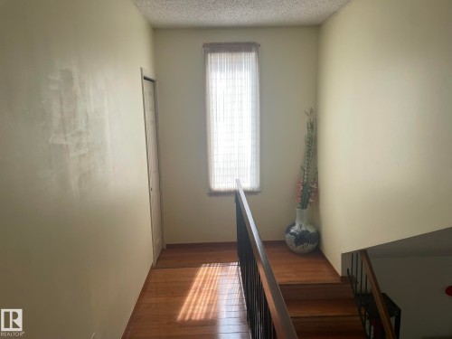 Hardwood flooring extending from the landing to the staircase, featuring a vertical window with privacy coverings and a built-in closet - 9320 175 Street, Edmonton, AB - Indoor Photo Showing Other Room