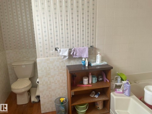 Bathroom featuring a built-in tub, white ceramic wall tiling, wood-finish flooring, and a commode - 9320 175 Street, Edmonton, AB - Indoor Photo Showing Bathroom