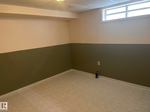 Finished lower level room featuring a drop ceiling, a single light fixture, a high horizontal window, two-tone painted walls, and light-toned tile flooring - 9320 175 Street, Edmonton, AB - Indoor