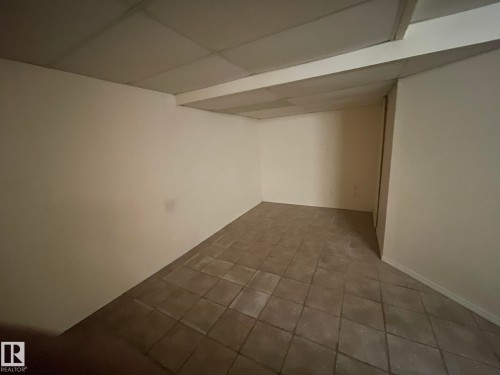 Spacious room featuring neutral-toned walls, square tile flooring, and a drop ceiling with integrated lighting - 9320 175 Street, Edmonton, AB - Indoor Photo Showing Other Room