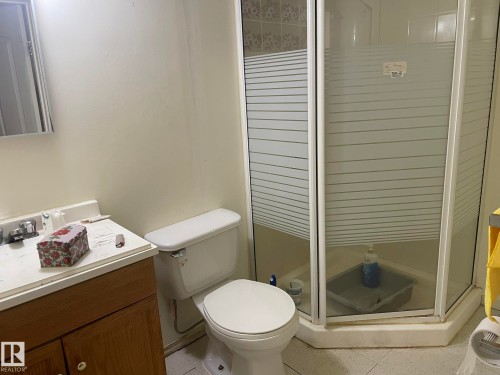 Bathroom featuring a corner shower enclosure with frosted glass panels, a white toilet, and a wood-finish vanity with a white countertop and integrated sink - 9320 175 Street, Edmonton, AB - Indoor Photo Showing Bathroom