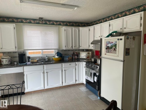 Kitchen featuring white cabinetry, granite-style countertops, tile flooring, a window above the sink, and a range with a range hood - 9320 175 Street, Edmonton, AB - Indoor Photo Showing Kitchen With Double Sink