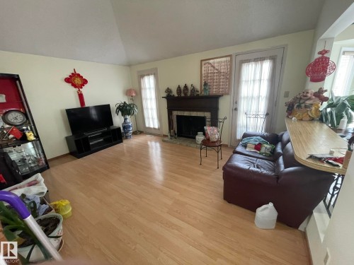 Living area featuring light wood-finish flooring, a vaulted ceiling, and a fireplace with a wood mantle - 9320 175 Street, Edmonton, AB - Indoor Photo Showing Living Room With Fireplace