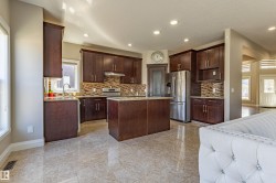 The kitchen features dark wood cabinetry, a central island, stainless steel appliances, and a tiled backsplash - 