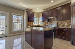 The kitchen features a functional island with a granite countertop, rich dark wood cabinetry, a tiled backsplash, and stainless steel appliances, including a range and range hood - 