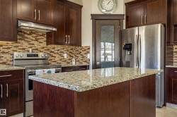 The kitchen features dark wood cabinetry, stainless steel appliances, a mosaic tile backsplash, and a central island with a granite countertop - 