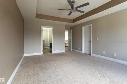 This room features a tray ceiling with a ceiling fan, carpeted flooring, and a white paneled door - 