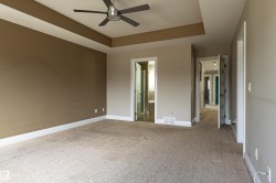 Spacious room featuring carpeted flooring, a tray ceiling with a ceiling fan, and access to a bathroom with a glass shower enclosure - 