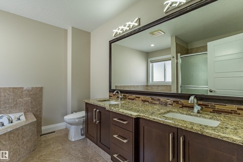 Bathroom featuring a double vanity with granite countertops and dark wood cabinetry, a tiled bathtub surround, and a mirror with overhead lighting - 3611 14 Street, Edmonton, AB - Indoor Photo Showing Bathroom