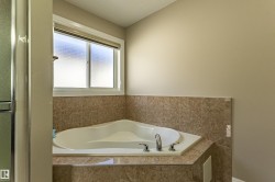 The bathroom features a corner soaking tub with a tiled surround and a window with a privacy film - 