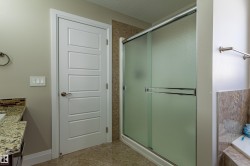 The bathroom features a glass-enclosed shower with a sliding door, a vanity with a granite countertop and mosaic tile backsplash, and a white paneled door - 