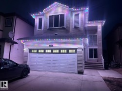 The property features a two-car garage with a panel door and windows, a paved driveway, and exterior siding - 