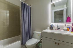 Bathroom featuring a modern vanity with an integrated sink, a lighted mirror, and a bathtub with tiled walls - 