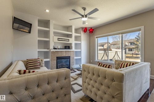 Living room featuring a fireplace with a stone surround, built-in shelving, and a ceiling fan - 3611 14 Street, Edmonton, AB - Indoor Photo Showing Living Room With Fireplace