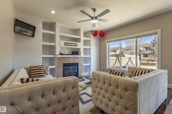 Living room featuring a fireplace with a stone surround, built-in shelving, and a ceiling fan - 