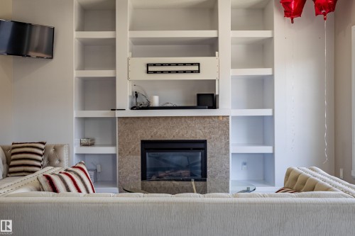 Living room featuring a fireplace with a stone surround, built-in shelving, and a wall-mounted television - 3611 14 Street, Edmonton, AB - Indoor Photo Showing Living Room With Fireplace