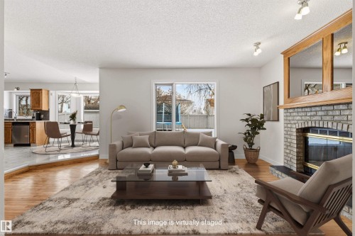 The living area features hardwood floors and a brick fireplace with a wood mantle - 3668 31A Street, Edmonton, AB - Indoor Photo Showing Living Room With Fireplace