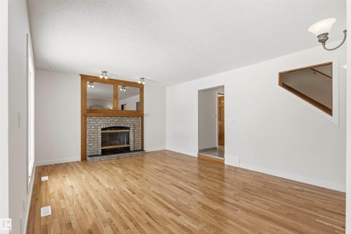 Living area featuring hardwood floors, a stone-faced fireplace with a wood mantel, and track lighting - 3668 31A Street, Edmonton, AB - Indoor Photo Showing Living Room With Fireplace