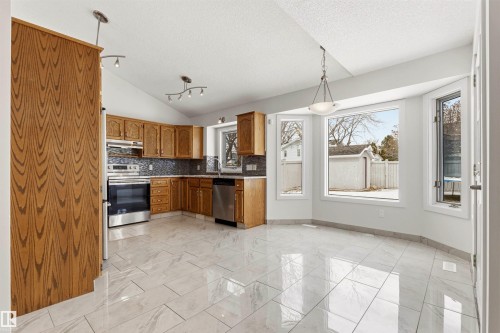 The kitchen features wood cabinetry, stainless steel appliances, and a tiled backsplash - 3668 31A Street, Edmonton, AB - Indoor Photo Showing Kitchen
