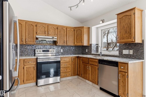 This kitchen features wood cabinetry, a tiled backsplash, and stainless steel appliances including a refrigerator, stove, and dishwasher - 3668 31A Street, Edmonton, AB - Indoor Photo Showing Kitchen