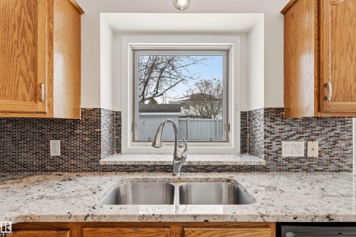 The kitchen features granite countertops, a stainless steel double basin sink with a gooseneck faucet, a mosaic tile backsplash, and wood cabinetry - 3668 31A Street, Edmonton, AB - Indoor Photo Showing Kitchen With Double Sink
