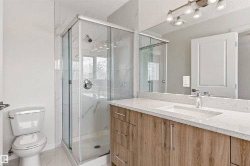 Bathroom featuring a glass-enclosed shower with white marble-patterned walls, a vanity with a light-colored countertop and a rectangular sink, and a large mirror with overhead lighting - 3668 31A Street, Edmonton, AB - Indoor Photo Showing Bathroom