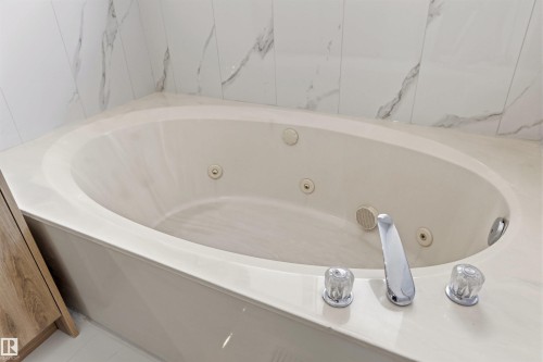 Bathroom featuring a built-in corner bathtub with jets, a chrome faucet, and marble-patterned wall tiles - 3668 31A Street, Edmonton, AB - Indoor Photo Showing Bathroom