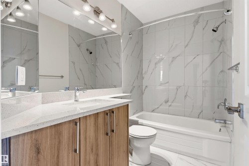 Bathroom featuring a vanity with a light-toned countertop and wood-look cabinetry, a built-in bathtub with an overhead shower, and white tiled walls - 3668 31A Street, Edmonton, AB - Indoor Photo Showing Bathroom