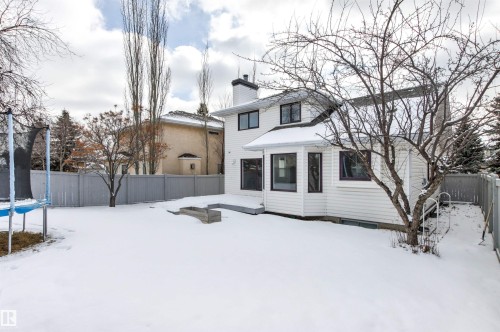 The property features an extensive yard with a snow-covered lawn, mature trees, and a wooden fence - 3668 31A Street, Edmonton, AB - Outdoor