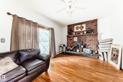 Living area featuring wood-finish flooring, a brick-surround fireplace with a stone hearth, a vaulted ceiling, a ceiling fan, and a large window - 