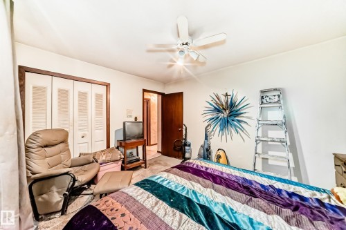 Interior room featuring a ceiling fan, white bi-fold closet doors with dark trim, and a dark wood-paneled door - 208 Willow Crescent, Wetaskiwin, AB - Indoor Photo Showing Bedroom