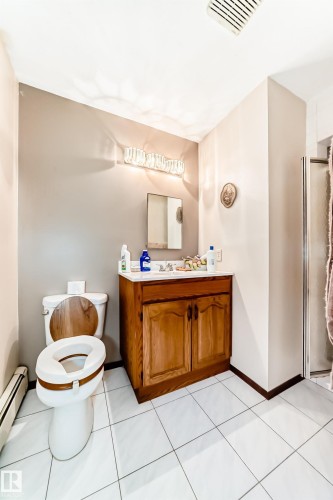 Bathroom featuring white square tile flooring, a wood-finish vanity with a white countertop, and a shower enclosure - 208 Willow Crescent, Wetaskiwin, AB - Indoor Photo Showing Bathroom