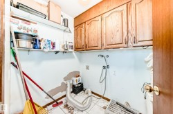 Utility room featuring wood cabinetry with metal hardware, white wall shelving, and white tiled flooring - 