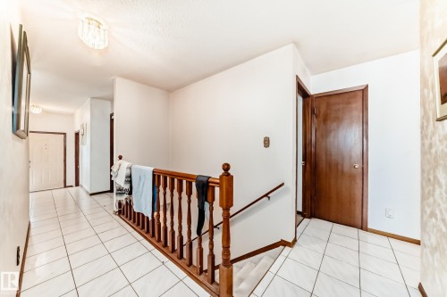 Open hallway featuring white ceramic tile flooring and a polished wood banister - 208 Willow Crescent, Wetaskiwin, AB - Indoor Photo Showing Other Room