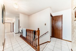 Open hallway featuring white ceramic tile flooring and a polished wood banister - 