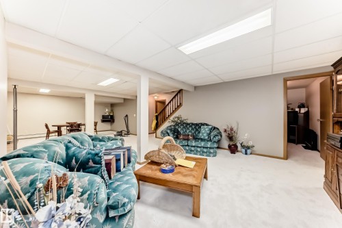 Expansive recreational space featuring a drop ceiling with integrated lighting, light-toned carpeting, and a visible wooden staircase - 208 Willow Crescent, Wetaskiwin, AB - Indoor