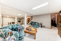 Expansive recreational space featuring a drop ceiling with integrated lighting, light-toned carpeting, and a visible wooden staircase - 