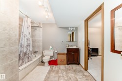 Bathroom featuring a tub/shower combination with light-toned wall tiles, a classic white toilet, and track lighting - 