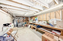 Unfinished basement featuring exposed ceiling joists, concrete flooring, a water heater, and a built-in workbench - 