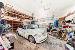 Spacious garage featuring a concrete floor, built-in shelving, two garage doors, and a ceiling-mounted skylight - 