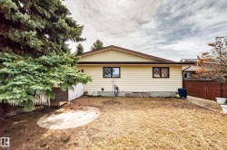 Rear exterior with light yellow siding and a brown roofline, featuring two windows with dark brown muntins - 